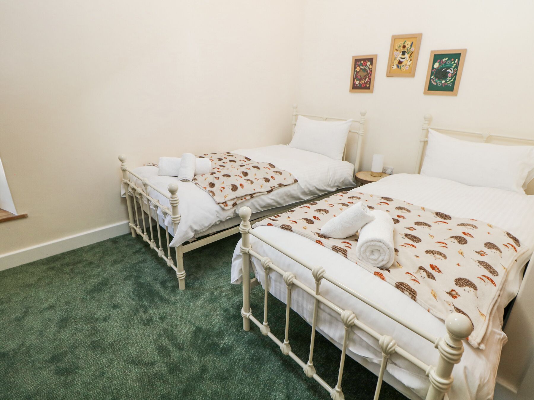 A double room with two beds, each with white bedding and a patterned blanket. There are three framed pictures on the wall.
