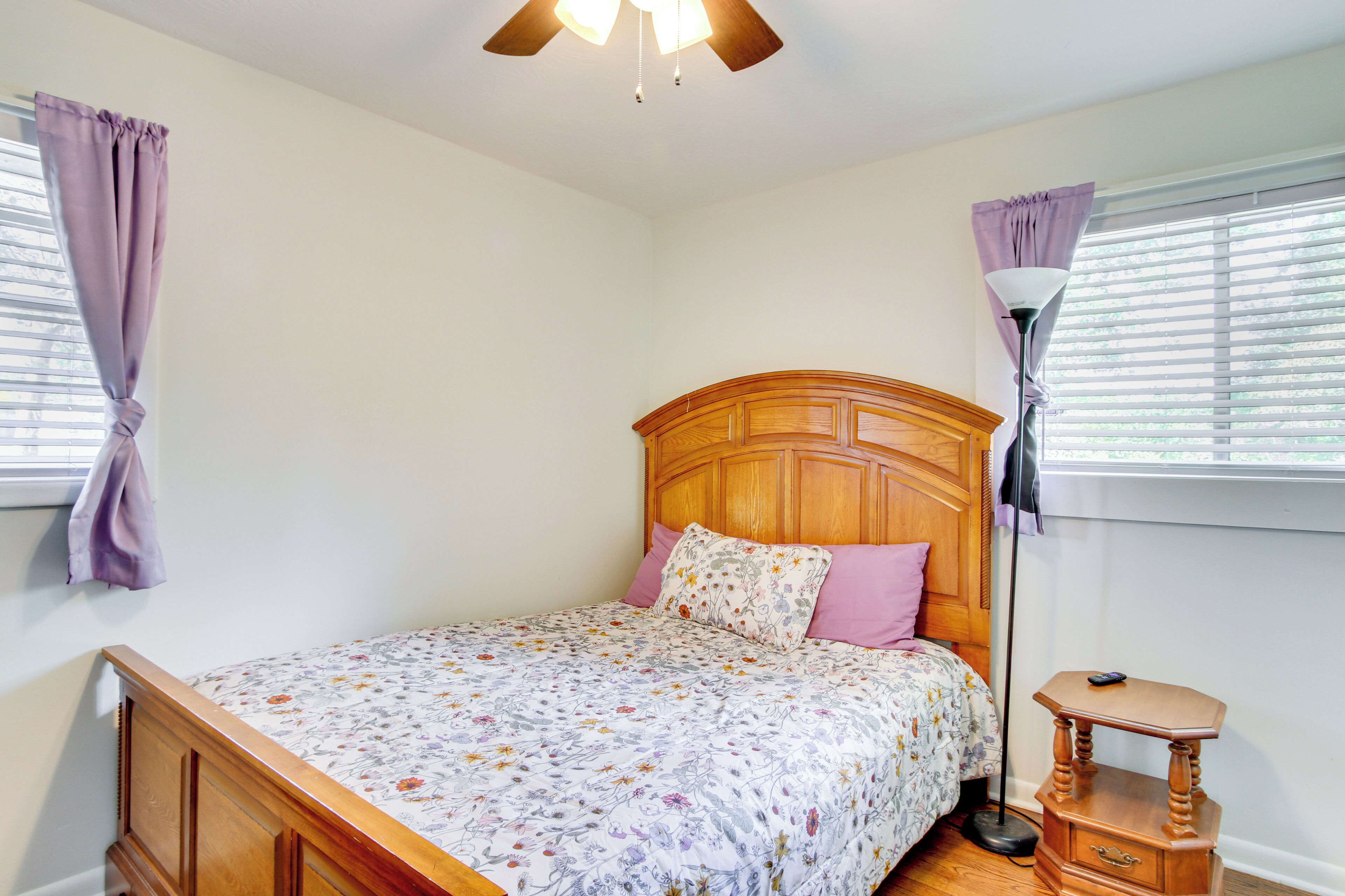Quarto com cama de madeira, roupa de cama floral, mesa de cabeceira e ventilador de teto.