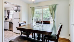Un coin repas avec une table et des chaises en bois, un ventilateur de plafond et une fenêtre avec des rideaux.