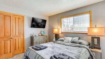 A bedroom with a bed, two bedside lamps, a TV, a window, and a wooden wardrobe.