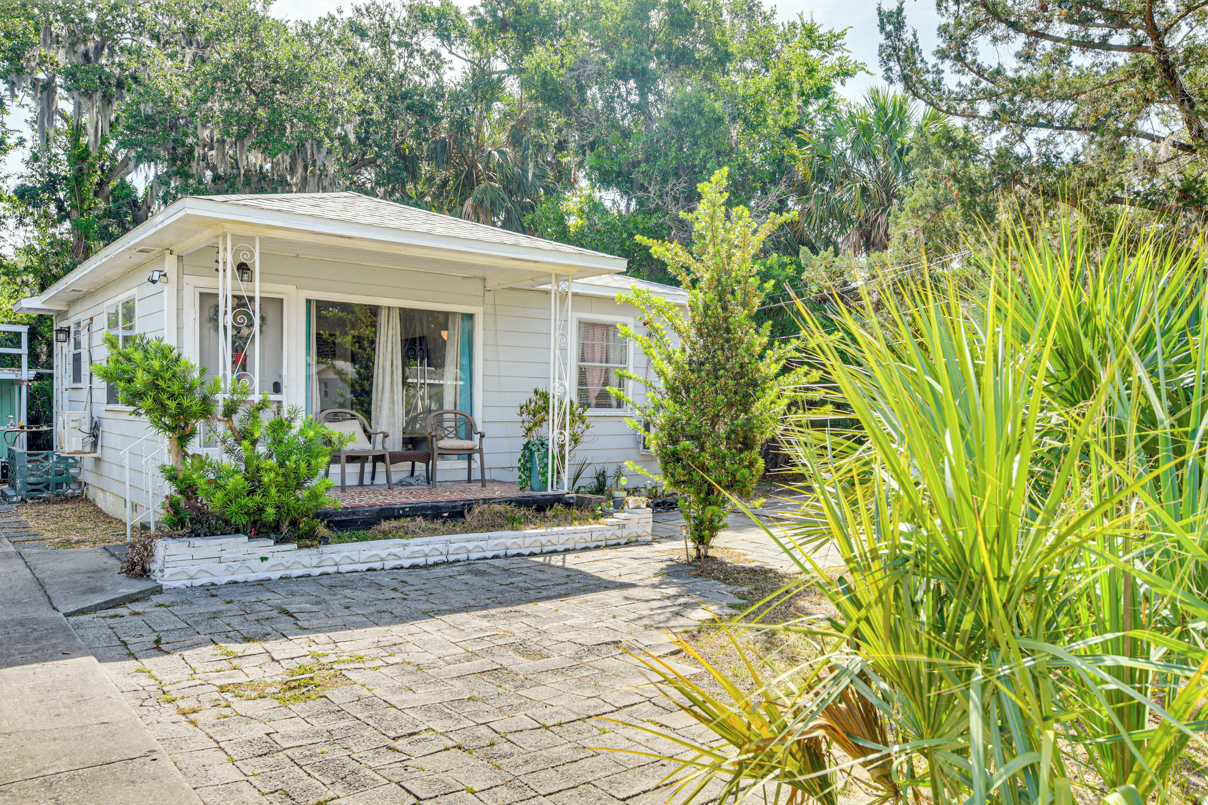 A white house with a porch, surrounded by greenery and trees.