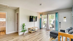 A living room with a wooden floor, a TV mounted on the wall, a sofa, and a small table with a plant. - 4 Mi to Daytona Boardwalk & Beaches: Cute Cottage (Holly Hill)