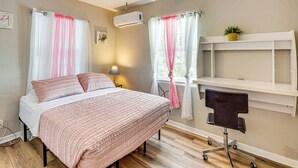 A bedroom with a bed, a ceiling fan, an air conditioner, a desk with a chair, and a window with curtains. - 4 Mi to Daytona Boardwalk & Beaches: Cute Cottage (Holly Hill)