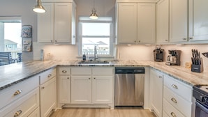 Una cocina moderna con armarios blancos, lavavajillas de acero inoxidable y encimera de mármol.