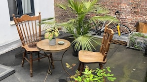 A small outdoor seating area with two wooden chairs and a round table, surrounded by potted plants and a bicycle.