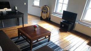 A living room with a sofa, a coffee table with flowers, a television, and a jukebox.