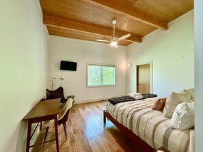 Ein Schlafzimmer mit Bett, Schreibtisch, Stuhl, Wand-Fernseher und Fenster.