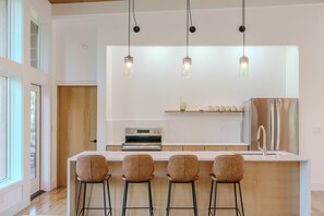 A modern kitchen with a central island, bar stools, stainless steel appliances, and pendant lighting.
