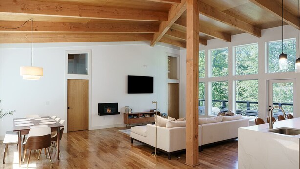Un amplio salón con techo de madera, chimenea, televisor y ventanas grandes que ofrecen vistas al exterior.