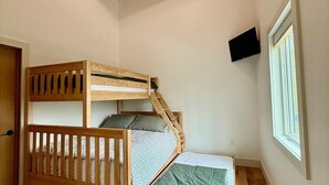Una habitación pequeña y acogedora con una cama litera, suelo de madera, techo inclinado con una lámpara, una ventana y un televisor montado.