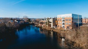 A riverside view of a modern building complex with multiple floors and a mix of brick and glass facades. - Cedar Tree House 319 (Traverse City)