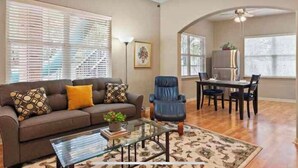 A living room with a sofa, coffee table, and a dining area with chairs and a table. - Clelia’s Cottage: Cozy 1-bedroom cottage in charming Austin with WiFi, AC (Austin)