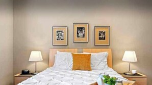 A hotel room with a large bed, two bedside tables, and three framed artworks on the wall. - Clelia’s Cottage: Cozy 1-bedroom cottage in charming Austin with WiFi, AC (Austin)