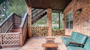 A covered outdoor area with a brick wall, a staircase, a wooden bench, and a green sofa. - Clelia’s Cottage: Cozy 1-bedroom cottage in charming Austin with WiFi, AC (Austin)
