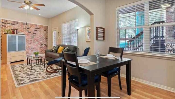 A dining area with a brick wall, a ceiling fan, and a large window with blinds. - Clelia’s Cottage: Cozy 1-bedroom cottage in charming Austin with WiFi, AC (Austin)