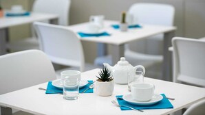 Un comedor con mesas y sillas blancas, cada juego con una tetera blanca, taza, platillo y una pequeña maceta.