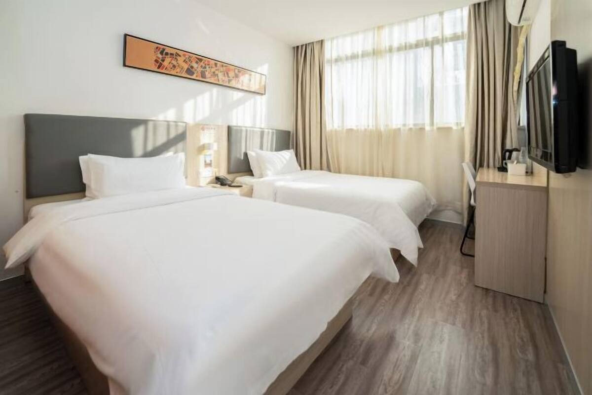 A hotel room with two beds, a flat-screen TV, a desk, and a painting on the wall.