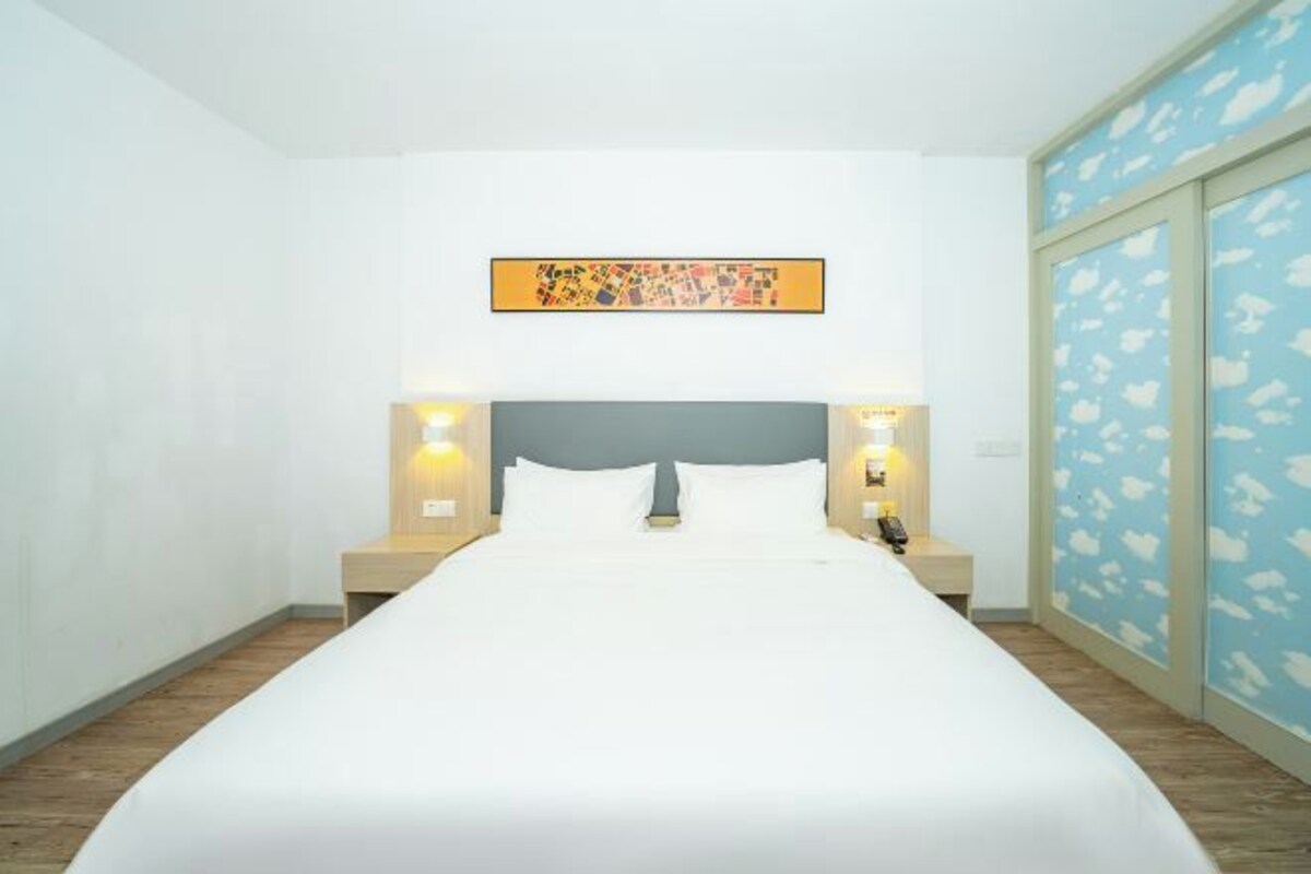 Une chambre d’hôtel avec un grand lit, une tête de lit, des tables de chevet et une œuvre d’art accrochée au mur.