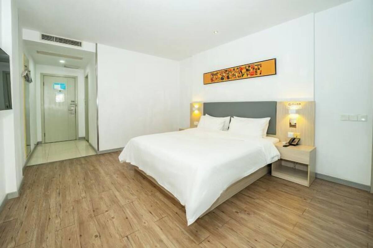 A hotel room with a large bed, bedside lamps, a headboard, a door, and a wall-mounted artwork.