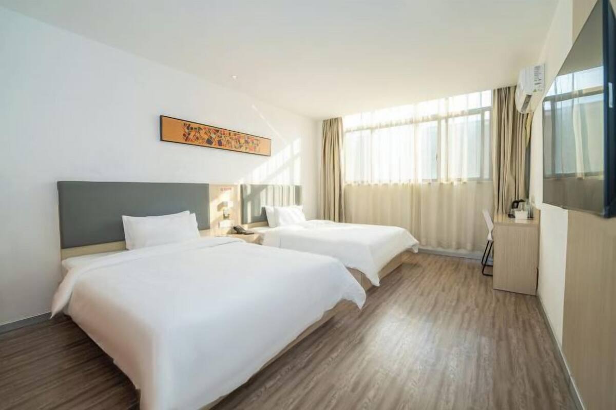 A hotel room with two beds, a desk, a chair, a TV, and a window with curtains.