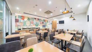 A modern dining area with multiple tables and chairs, a kitchen in the background, and a colorful mural on the wall.