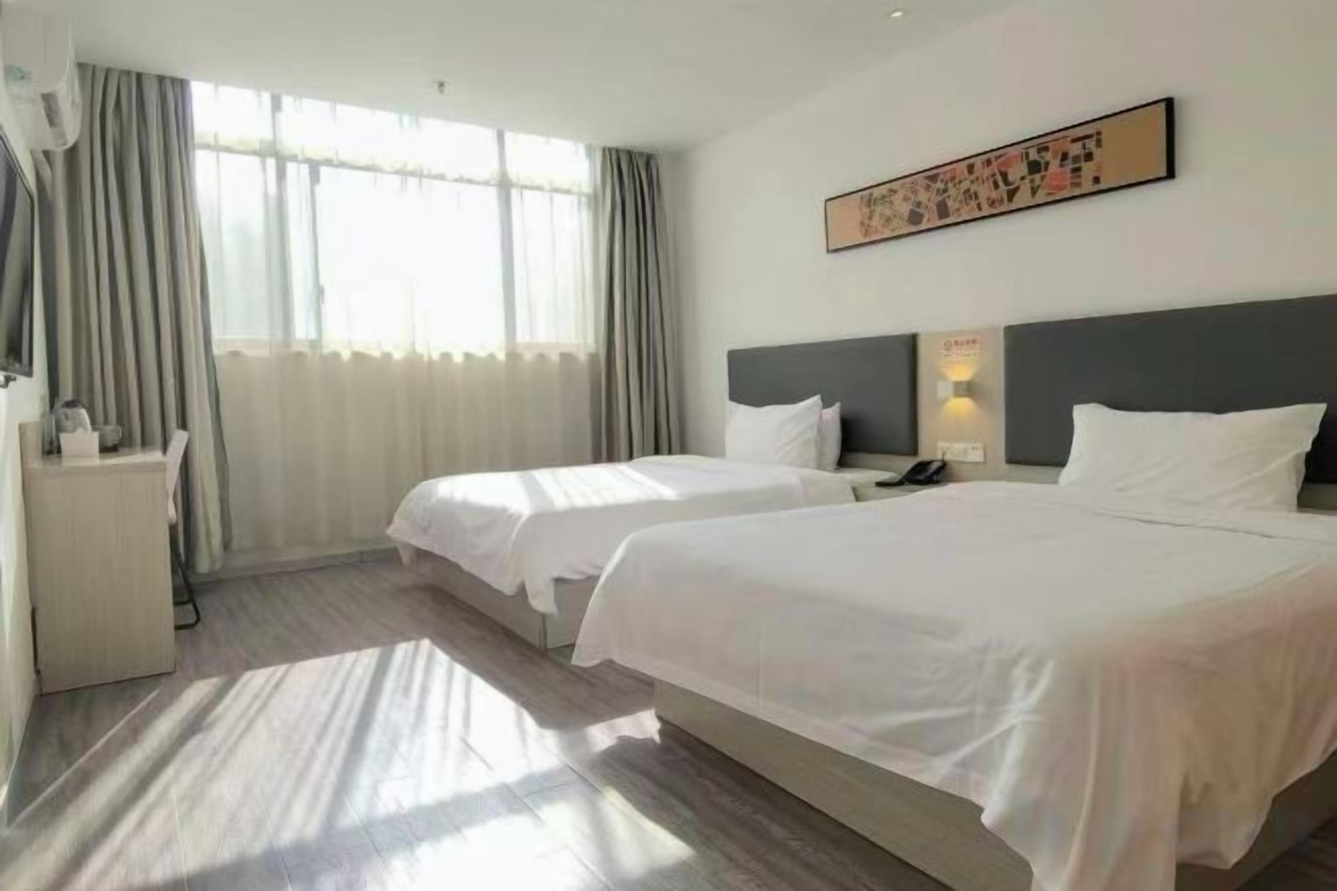 A hotel room with two beds, a desk, and a window with curtains.