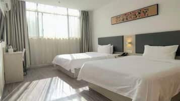A hotel room with two beds, a desk, and a window with curtains.