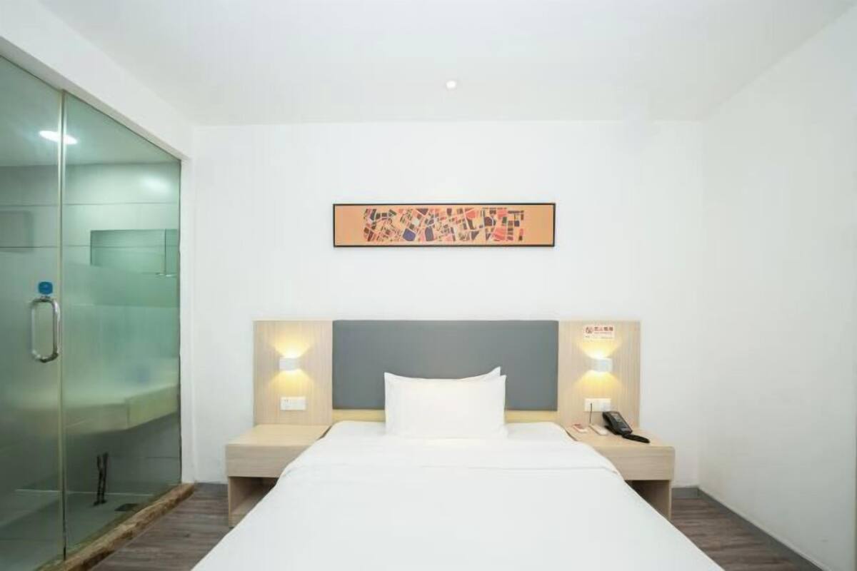 A hotel room with a bed, bedside tables, a glass shower enclosure, and a framed artwork on the wall.