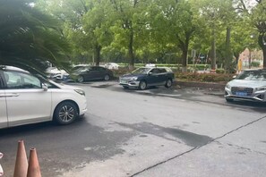 Un parking où sont garées plusieurs voitures, avec des arbres en arrière-plan et un bâtiment doté d’un toit rouge.