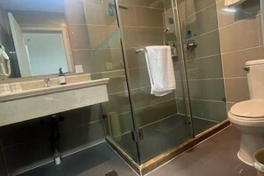 Kylpyhuone, jossa on lasiseinäinen suihkukaappi, wc ja peilillä varustettu pesuallas.