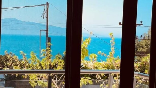 A balcony with a table and chairs, overlooking a coastal view with vegetation and a distant shoreline. - FAMILY INN Apartments (Sarande)