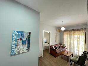 A living room with a sofa, coffee table, and a chair. There is a painting on the wall and a window with curtains. - FAMILY INN Apartments (Sarande)