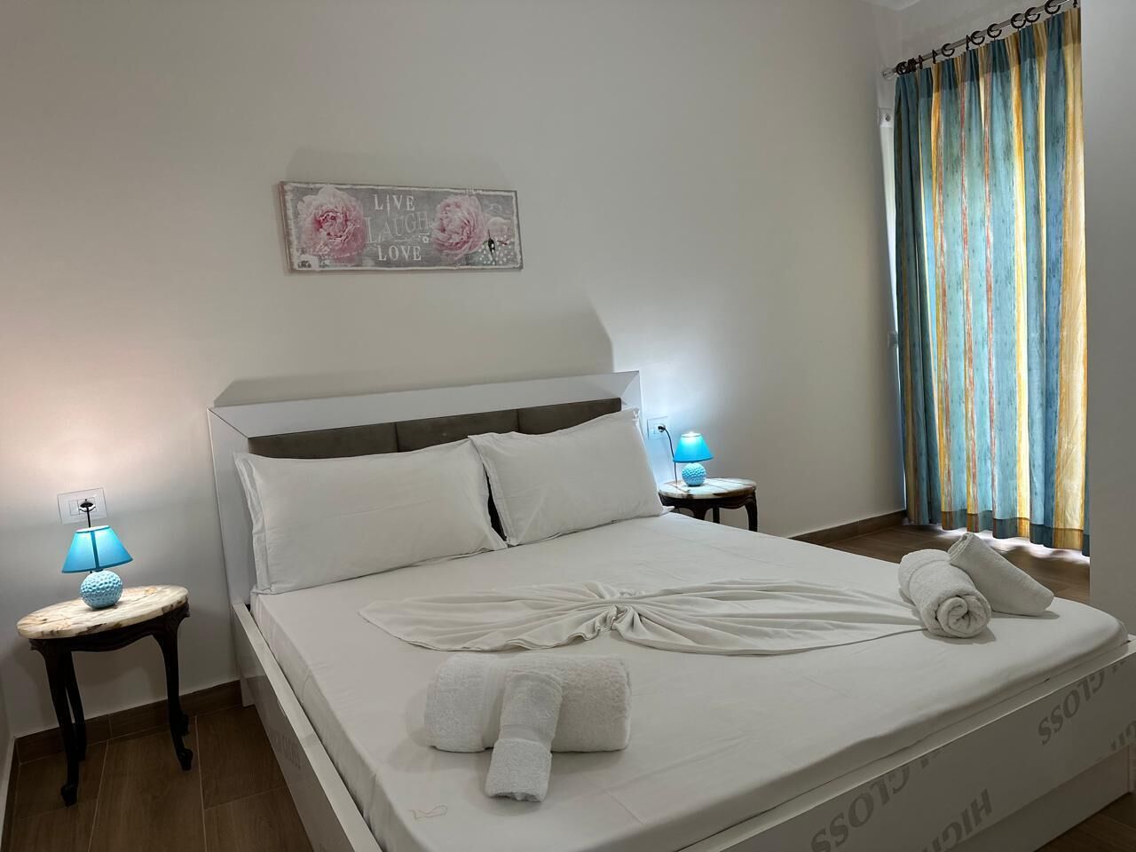 A neatly made bed with towels, a bedside lamp, and a decorative sign on the wall.