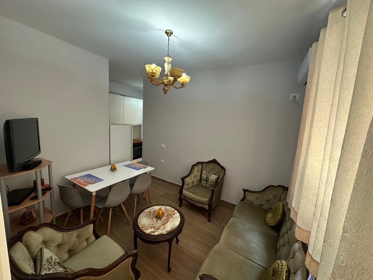 A living room with a television, dining table, chairs, a sofa, and a chandelier.