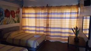 A hotel room with a bed, a small table with a plant, and a window with striped curtains. - Hotel Angel del mar (Puerto Ángel)