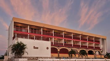 Um hotel de vários andares com telhado plano, várias varandas e uma área de recepção.