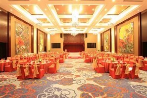 A banquet hall with rows of tables, a stage, and a carpeted floor.