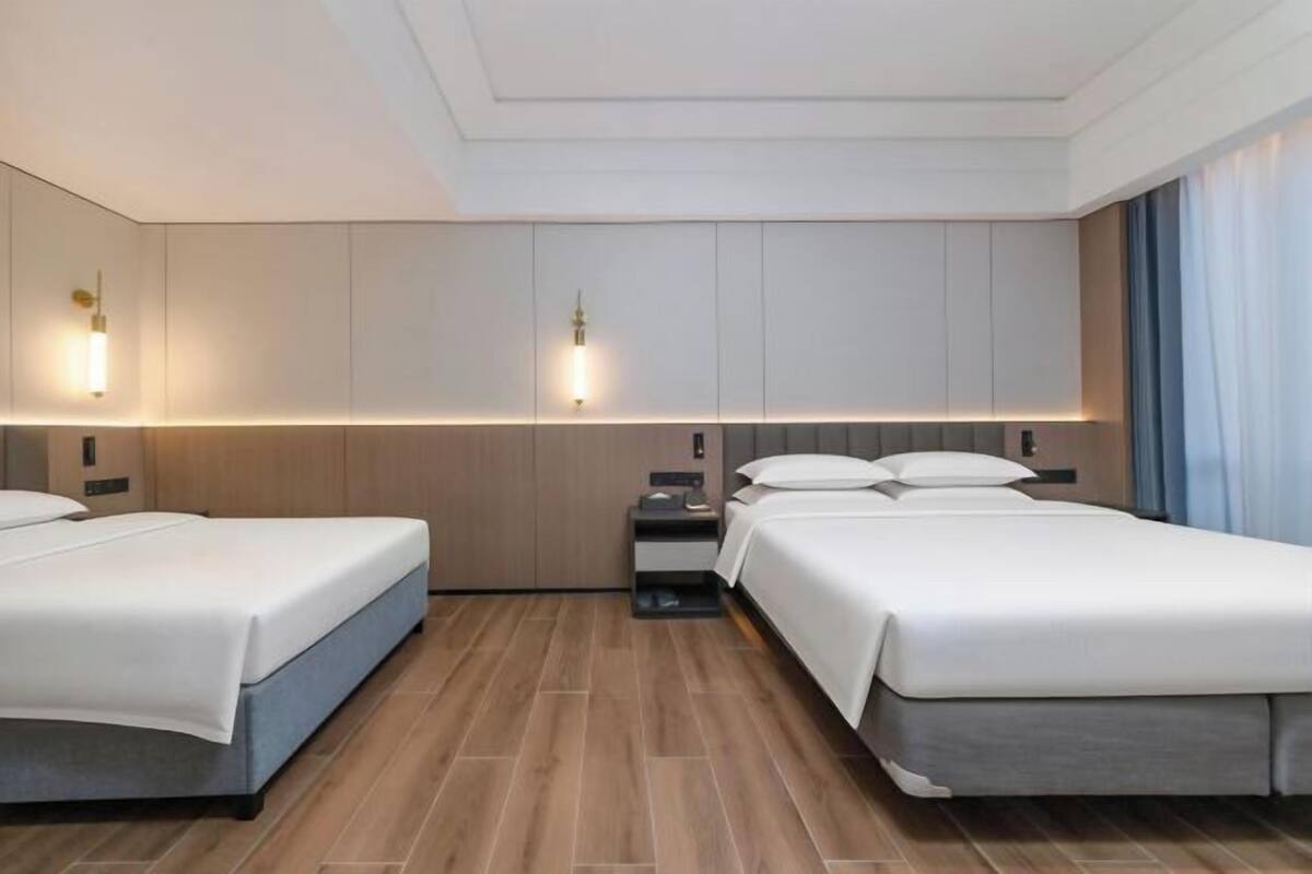 Une chambre d’hôtel avec deux lits, une table de chevet, une lampe fixée au mur et un plancher en bois.