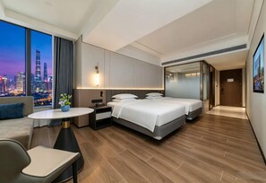Una habitación de hotel moderna con vista a la ciudad, una cama, un escritorio y un área de descanso.