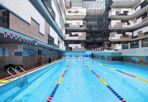 Une piscine intérieure avec des lignes de démarcation bien visibles, un poste de surveillance pour les sauveteurs et un mur carrelé orné d’une fresque.