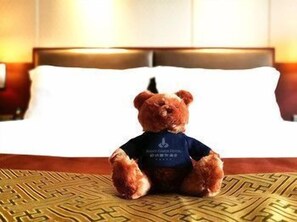 Ein Teddybär sitzt auf einem Bett mit einem gemusterten Überwurf.
