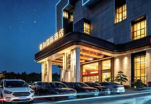 Un hotel con fachada moderna, varios espacios de estacionamiento y señalización iluminada.