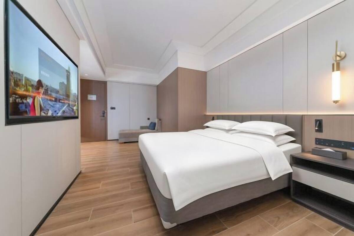 Une chambre d’hôtel moderne avec un grand lit, un téléviseur fixé au mur et une table de chevet.