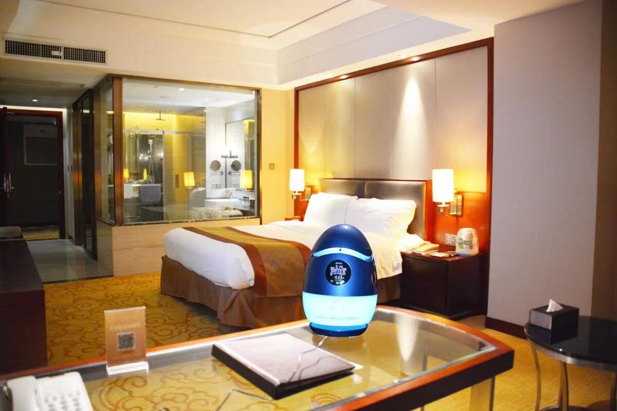 A hotel room with a bed, bedside tables, a mirror, and a glass partition.