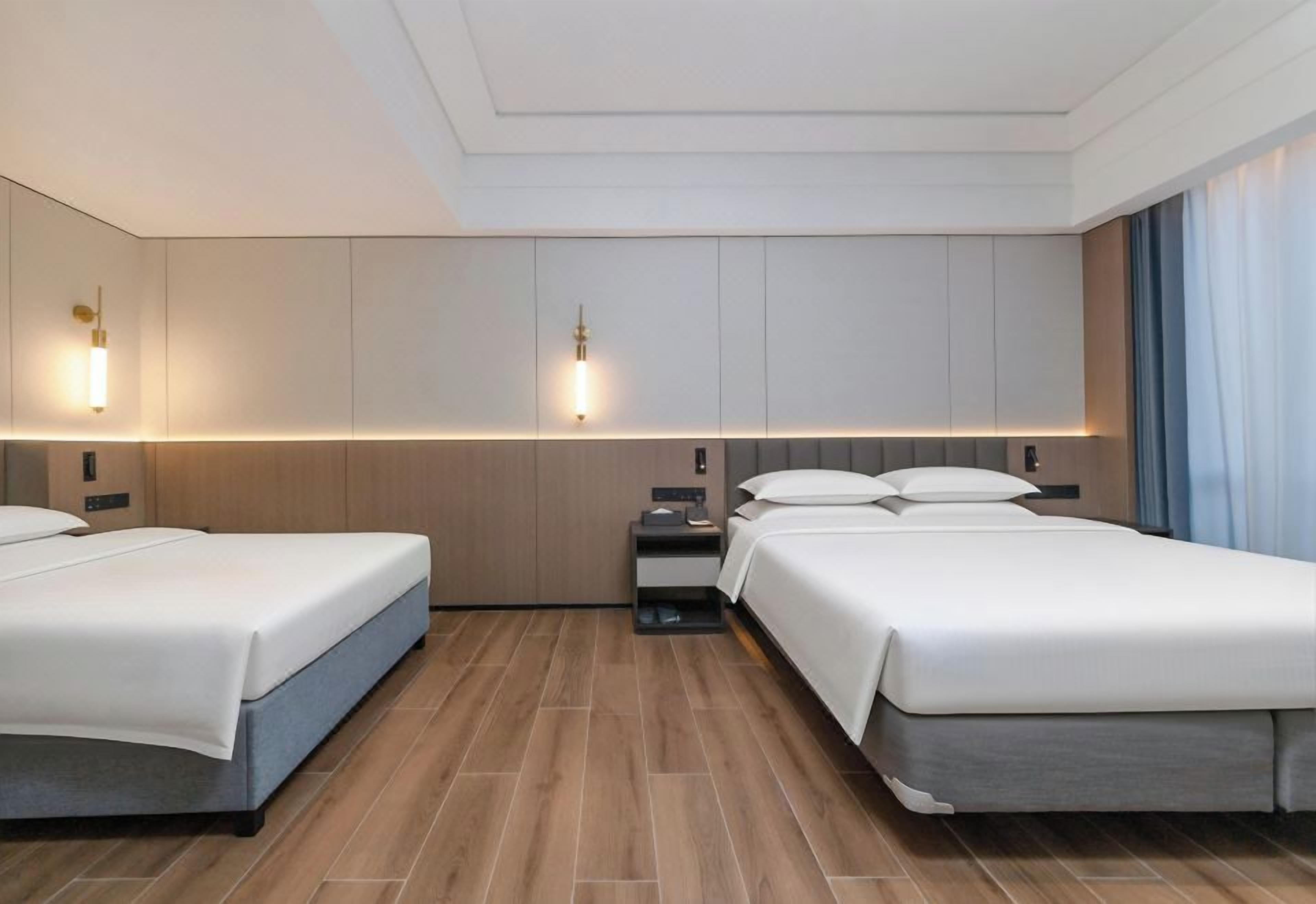 A hotel room with two beds, a nightstand, and wall-mounted lighting.