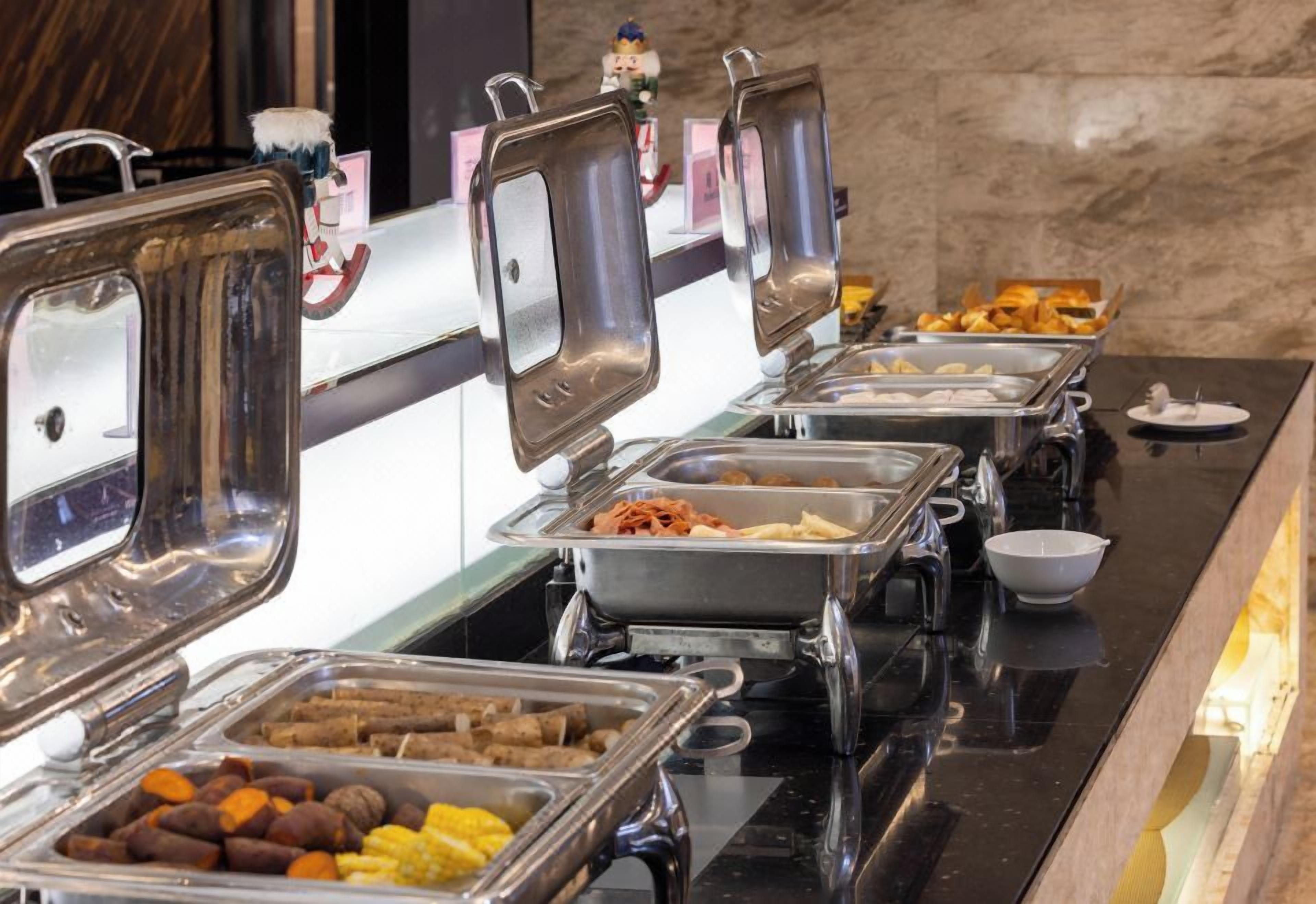 A buffet with various food items in metal containers, including meats, vegetables, and pastries.