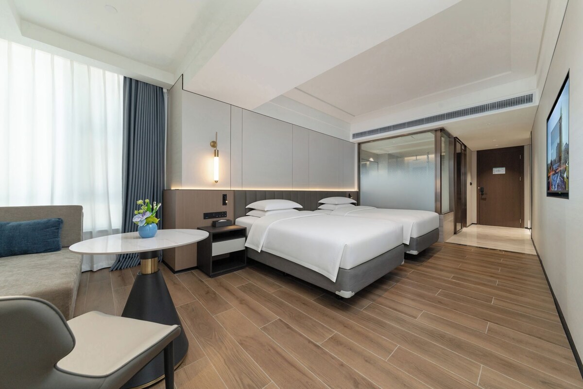 Una habitación de hotel moderna con una cama grande, una mesita de noche, un sofá y una pequeña mesa con un jarrón.
