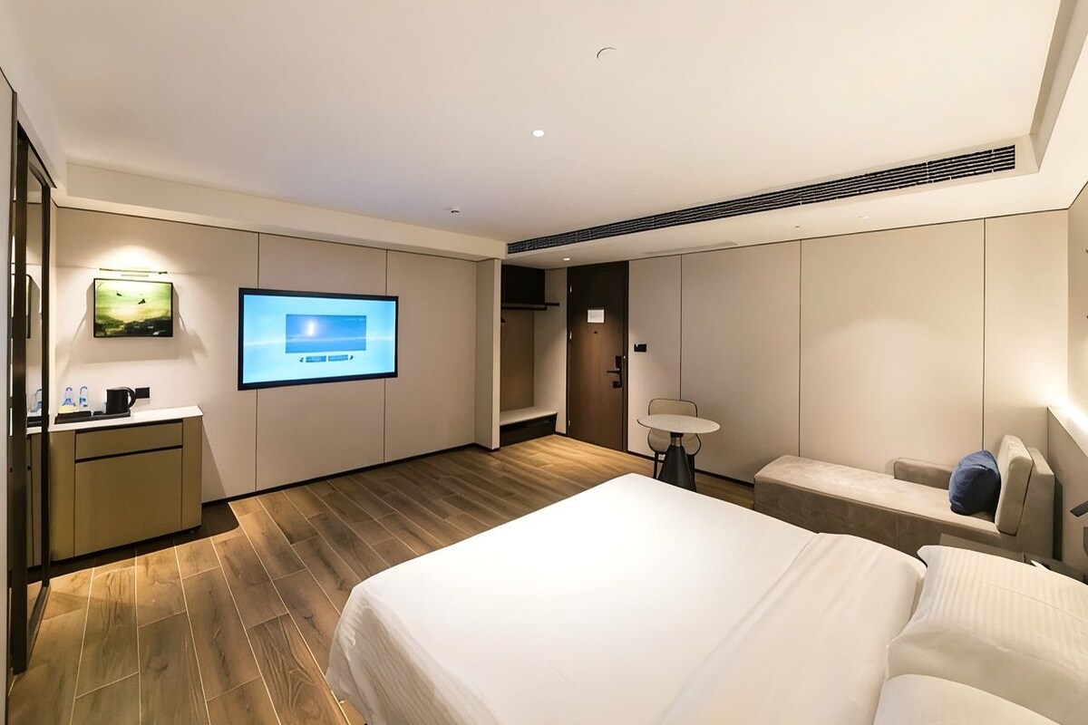 A hotel room with a bed, a desk with a computer, a TV, and a seating area.