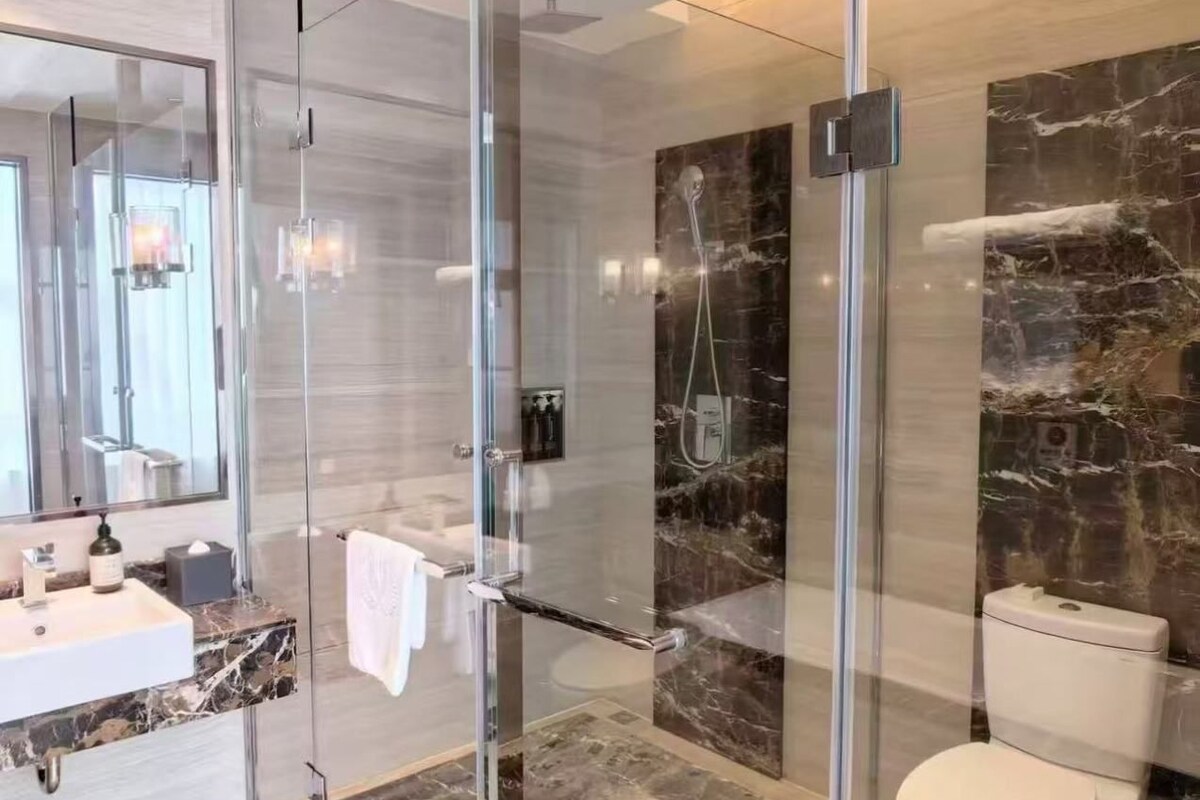 A modern bathroom with a glass-enclosed shower, a marble sink, and a toilet.