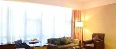 A hotel room with a sofa, a chair, a small table, and a lamp.